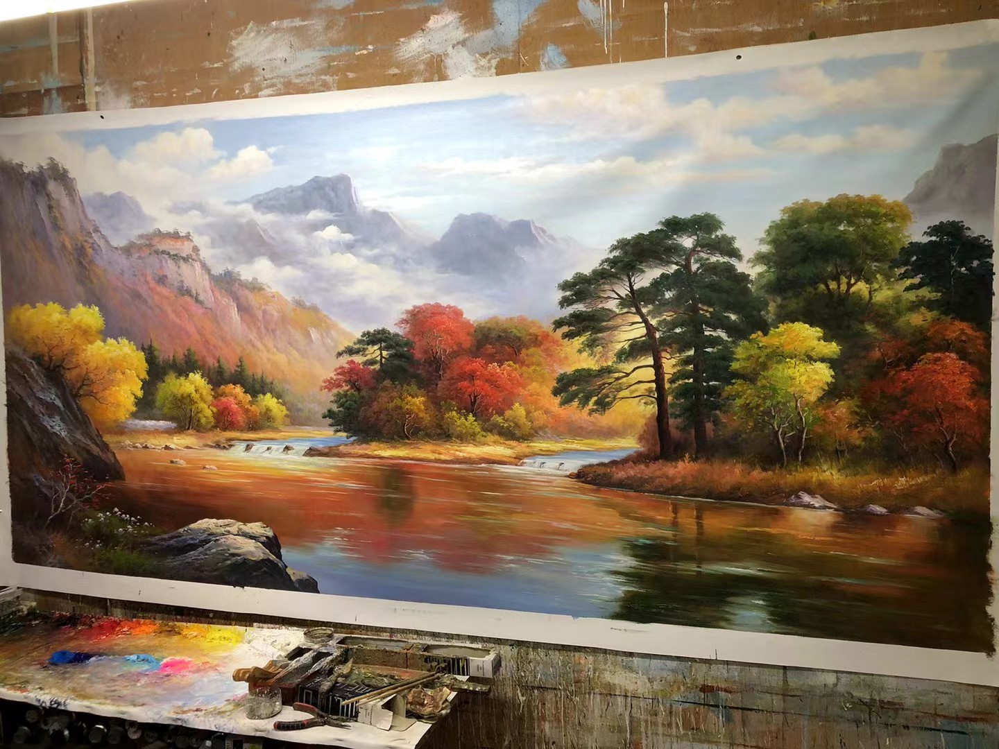 老廖画室调色台实拍，颜料一管管排开，正在绘制《金秋河谷》，画师现场创作沟通有底气
